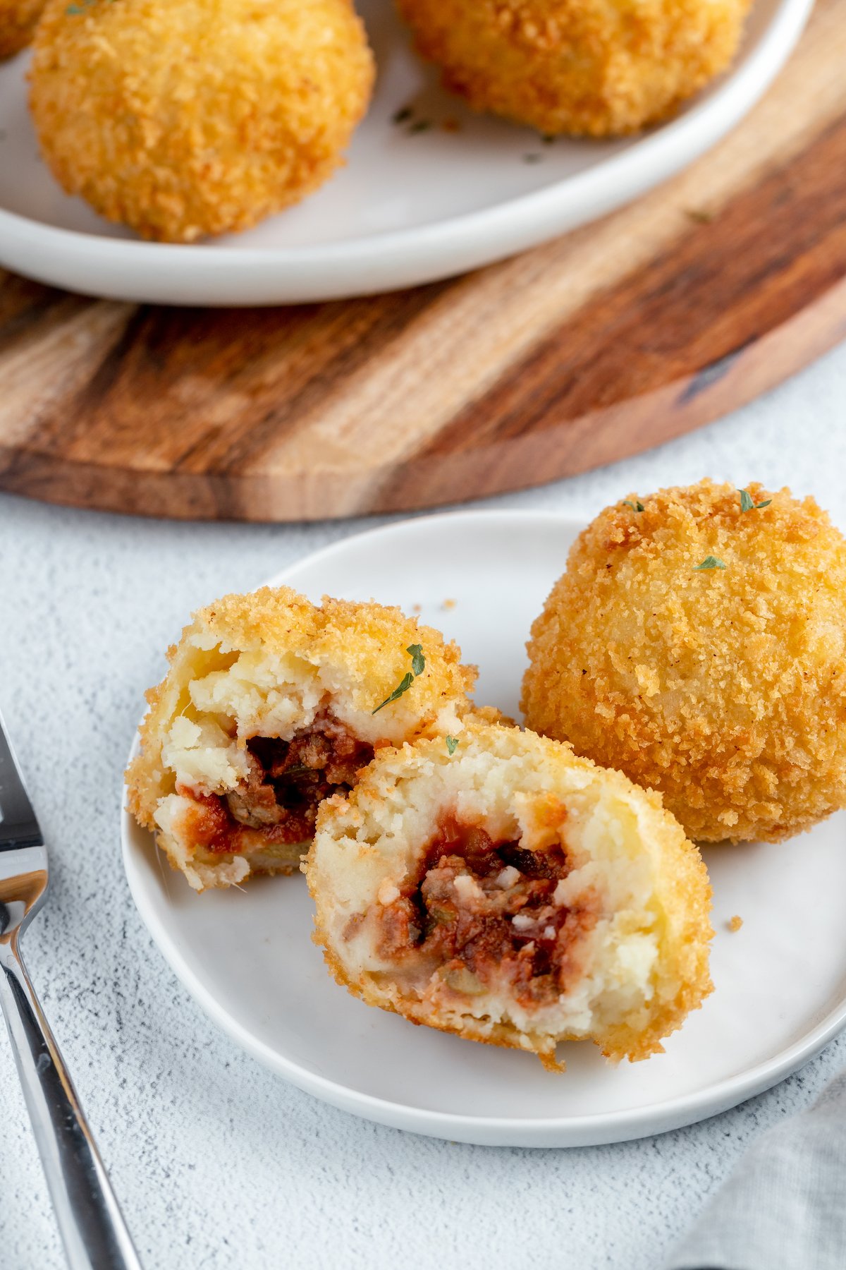 Two papas rellenas on a small plate. One has been broken apart to show the filling.