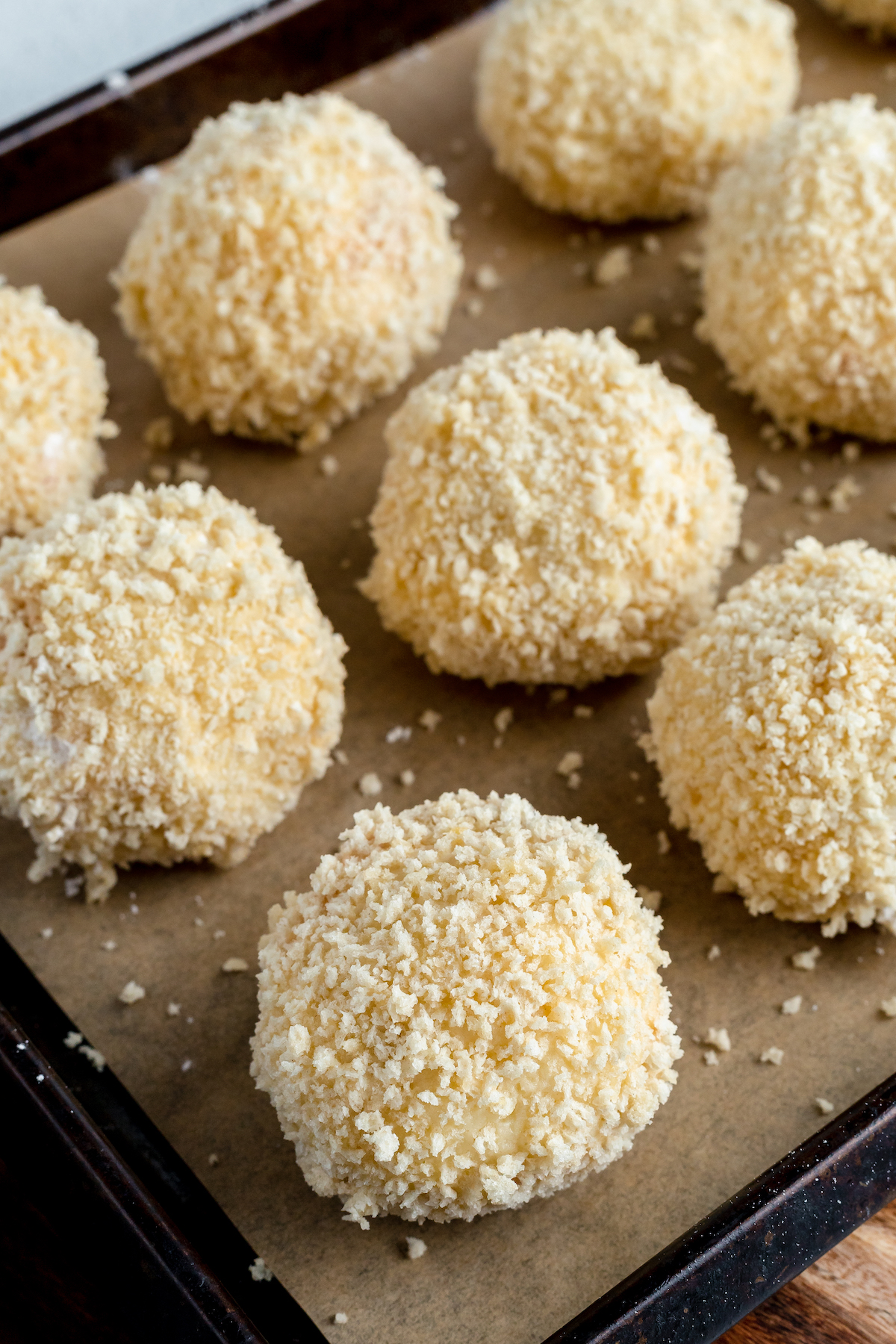 Close-up shot of breaded, un-fried mashed potato appetizers on a baking sheet, ready for frying.