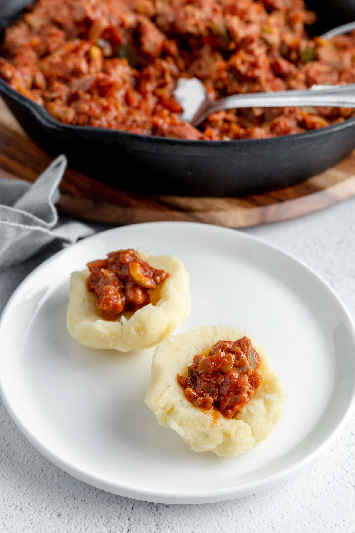 Two small mashed potato dumplings, filled with picadillo, ready to be topped with more mashed potato.