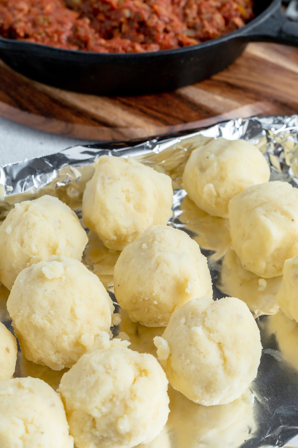 Balls of mashed potato on a foil-lined baking sheet.
