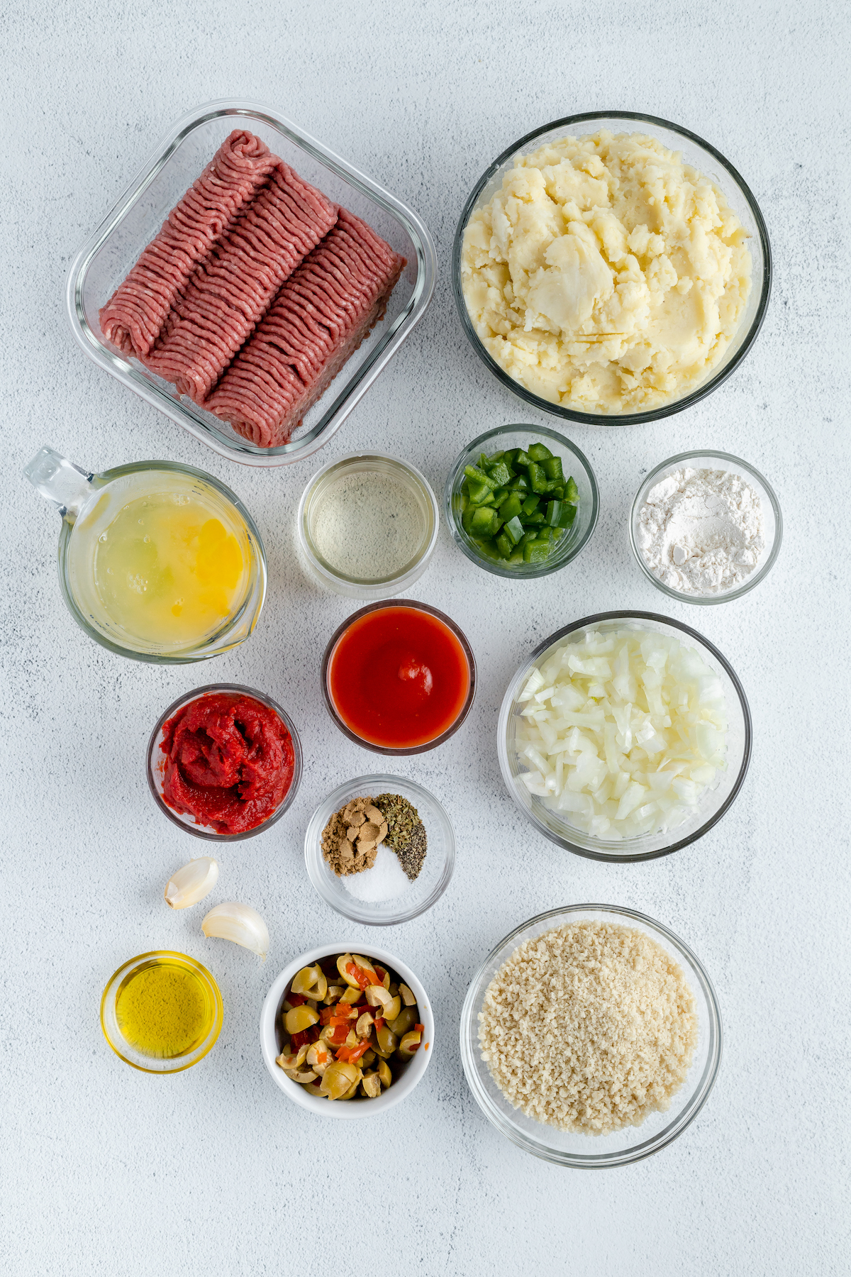 From top: Ground beef, mashed potatoes, egg yolks, egg whites, diced bell pepper, white wine, tomato paste, tomato sauce, diced onion, garlic, seasonings, olive oil, sliced green olives, bread crumbs.