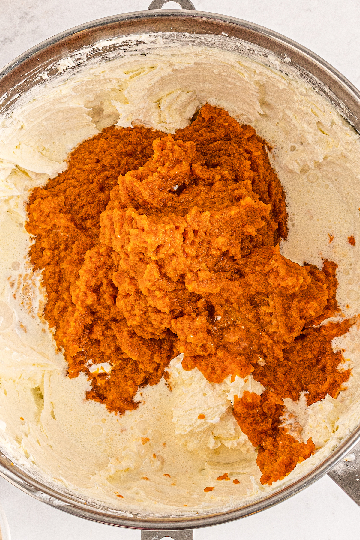 A whipped cream cheese mixture with pumpkin puree being added.