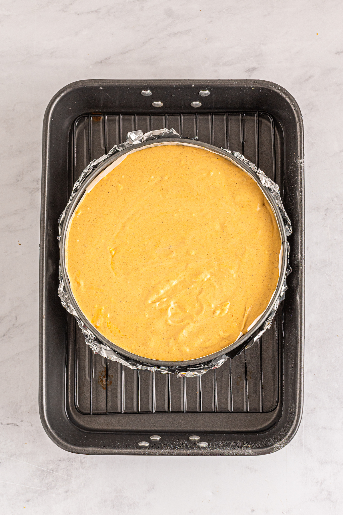 A baking pan partially filled with water, with a springform pan of unbaked cheesecake.