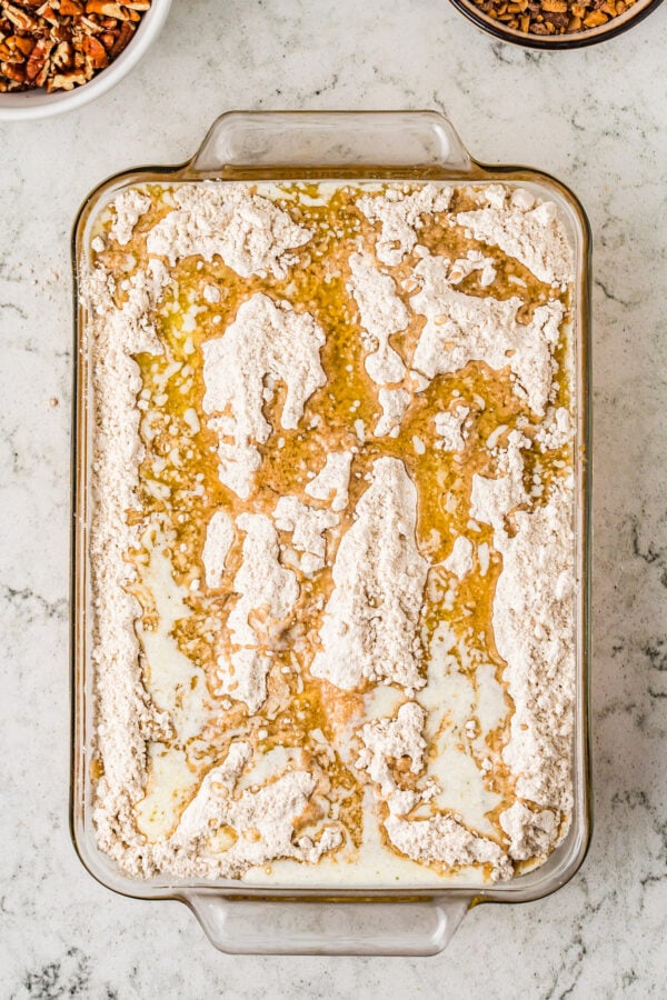 A rectangular glass baking dish filled with batter, cake mix, and melted butter.