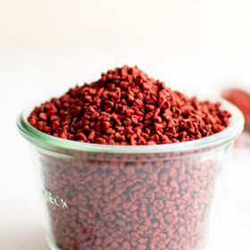 A cup overflowing with bright red annatto seeds.
