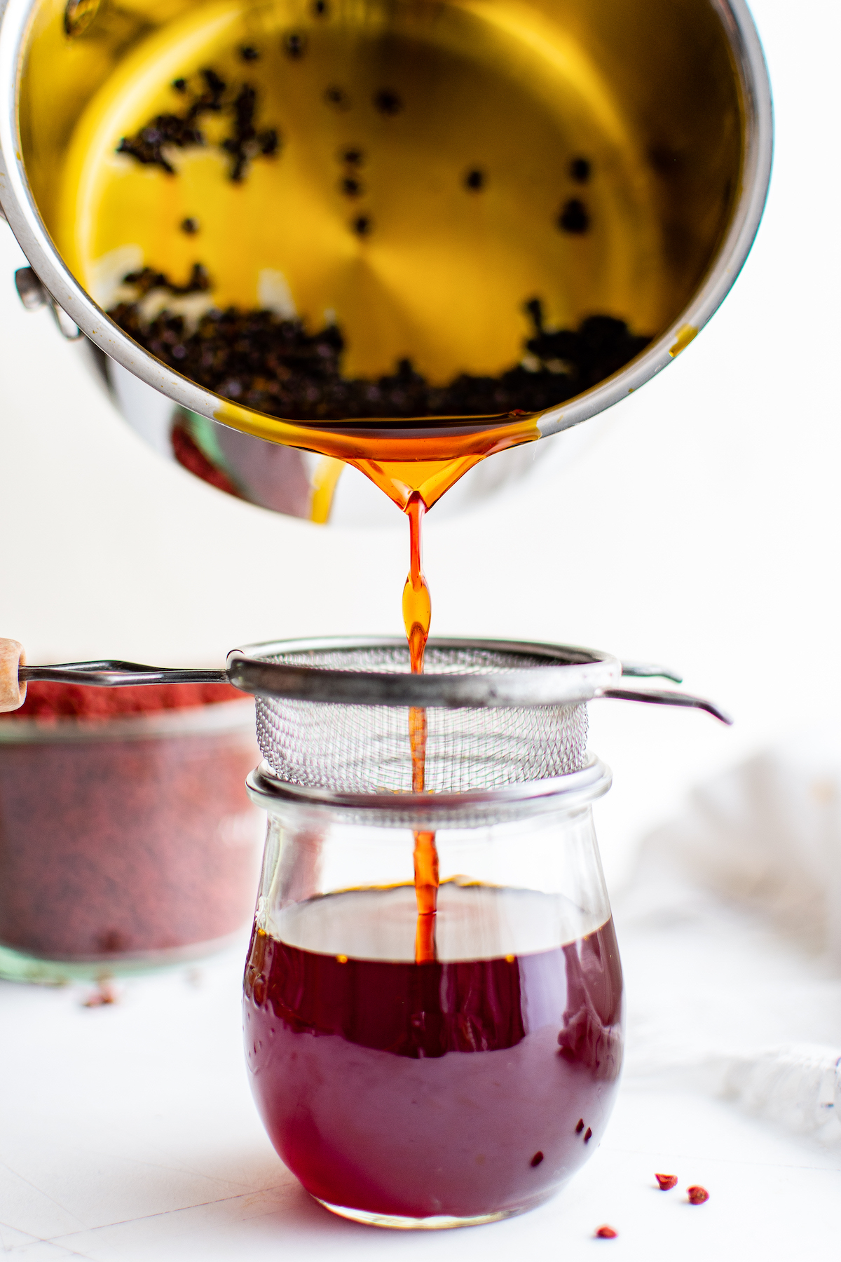 Achiote oil being poured into a small jar, through a fine mesh sieve.