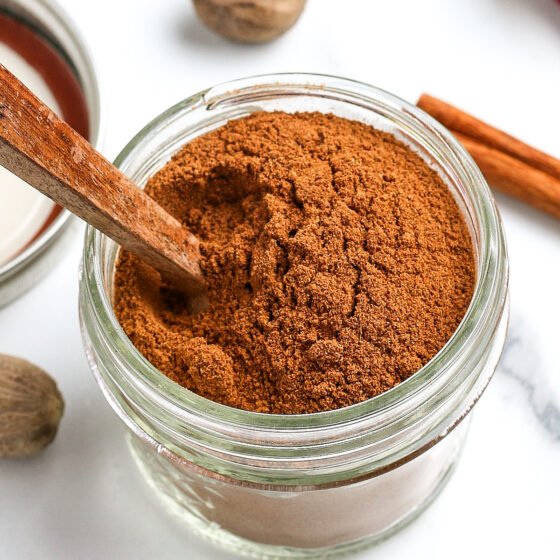 A small jar of apple pie spice with a small wooden spoon stuck into the jar.