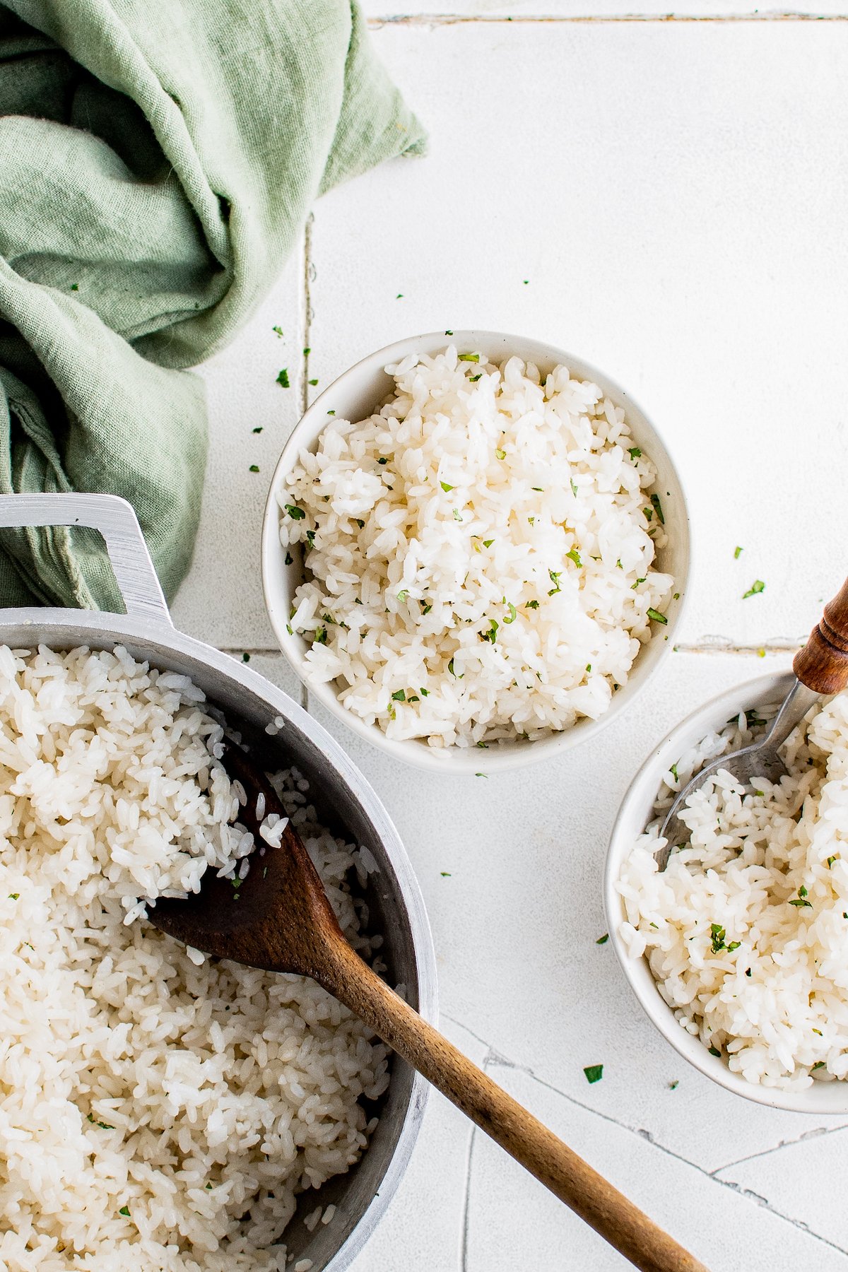 fluffy white rice in a bowl garnished with fresh herbs next to a dutch oven with rice as well