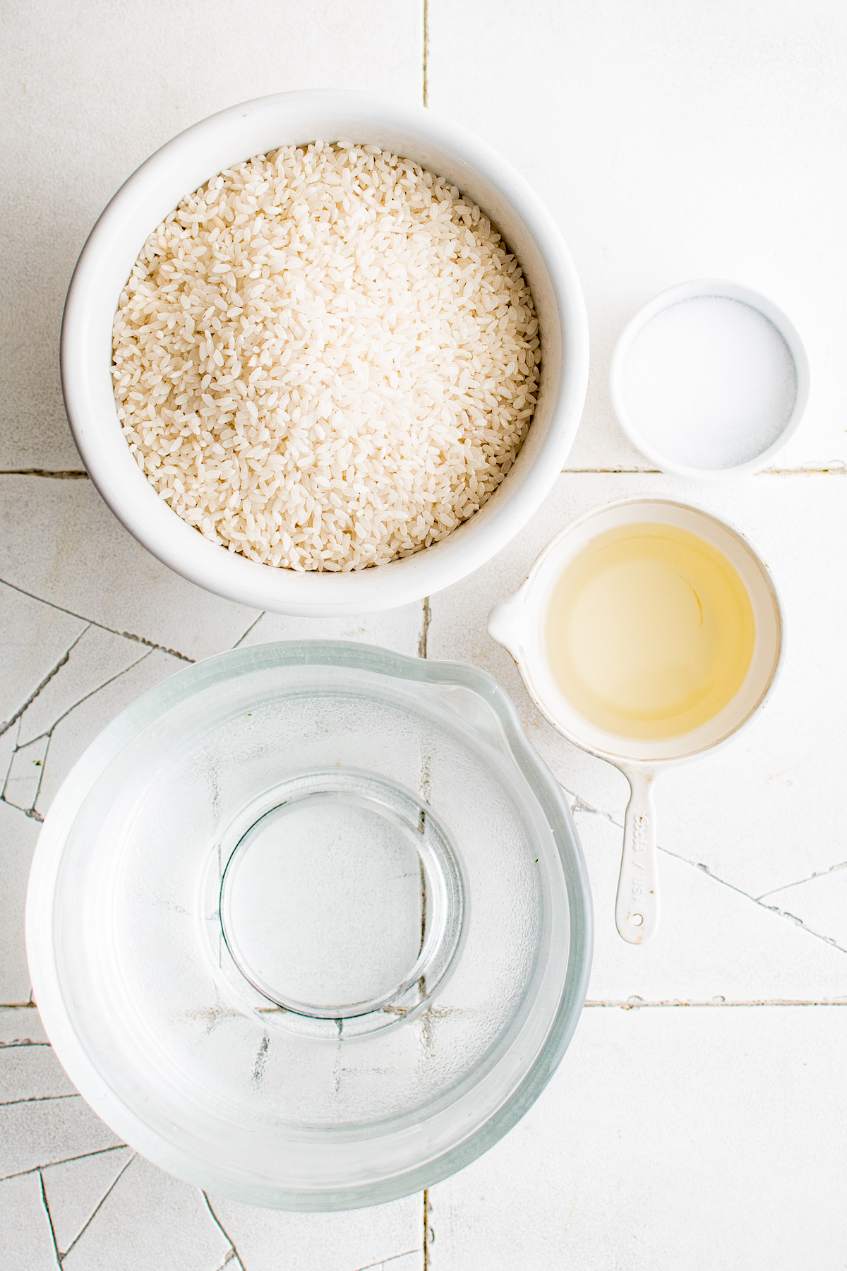 ingredients to cook rice including individual bowls of rice, water, salt, and cooking oil