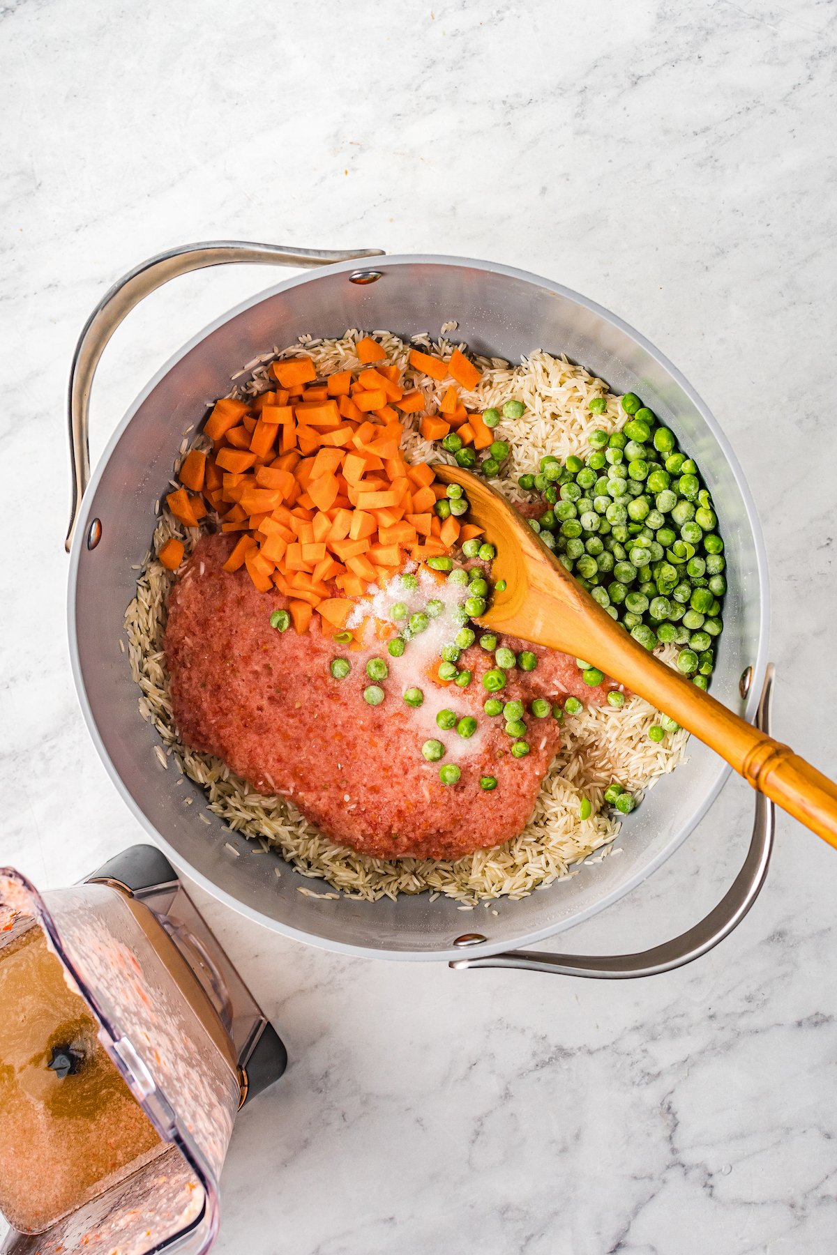 Toasted rice, tomato puree, carrots, and peas cooking in a saucepan.
