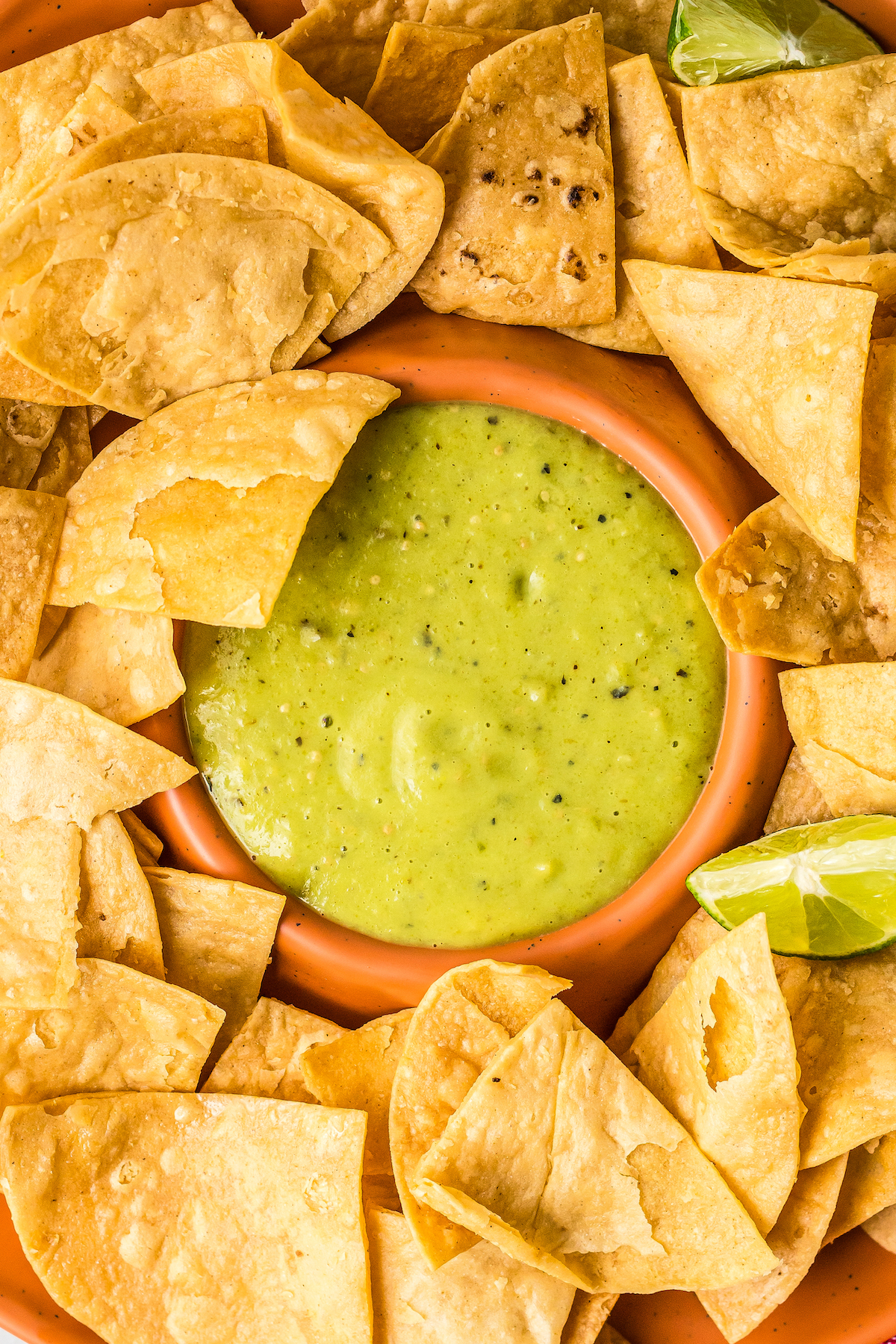 Avocado salsa in an orange dip bowl, surrounded by fried tortilla chips.