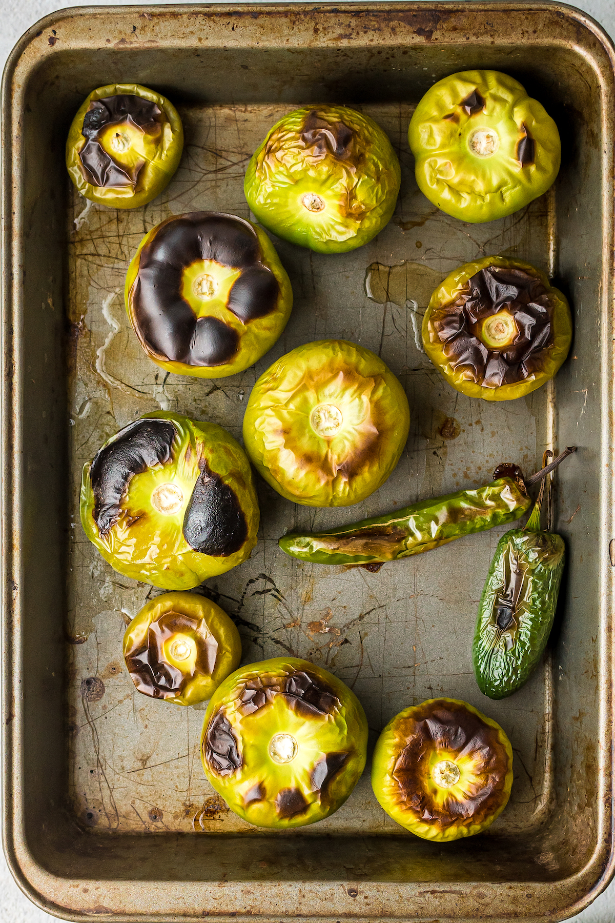 Roasted tomatillos and peppers on a baking sheet.