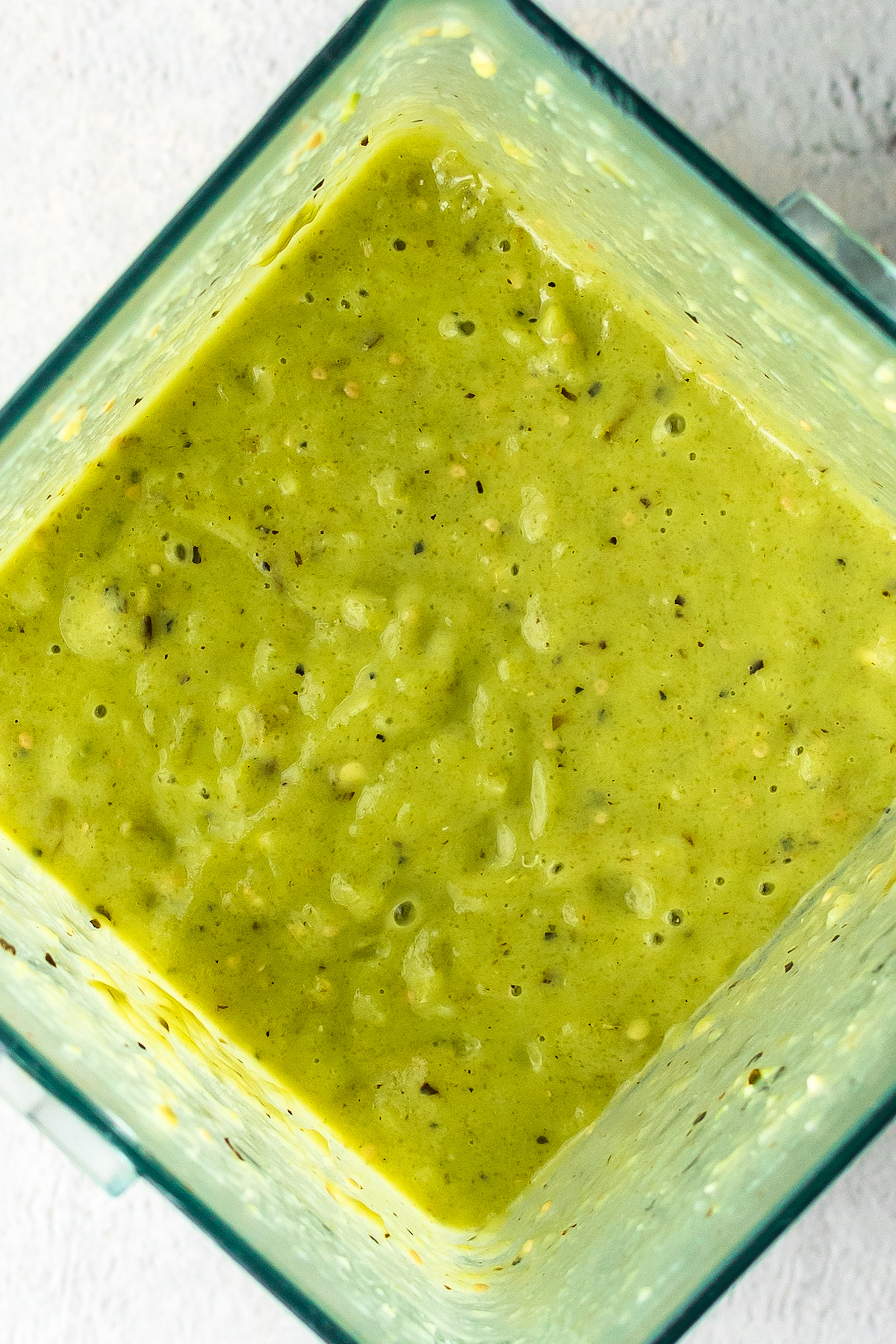 Overhead shot of a blender filled with creamy, blended, green salsa.