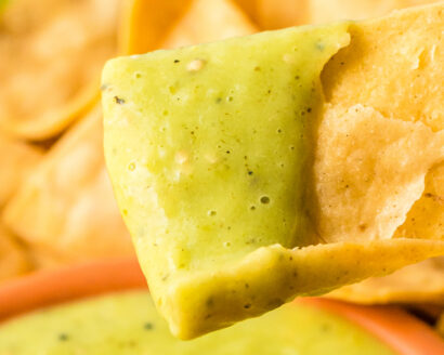 Close-up shot of a tortilla chip dipped in creamy avocado salsa.
