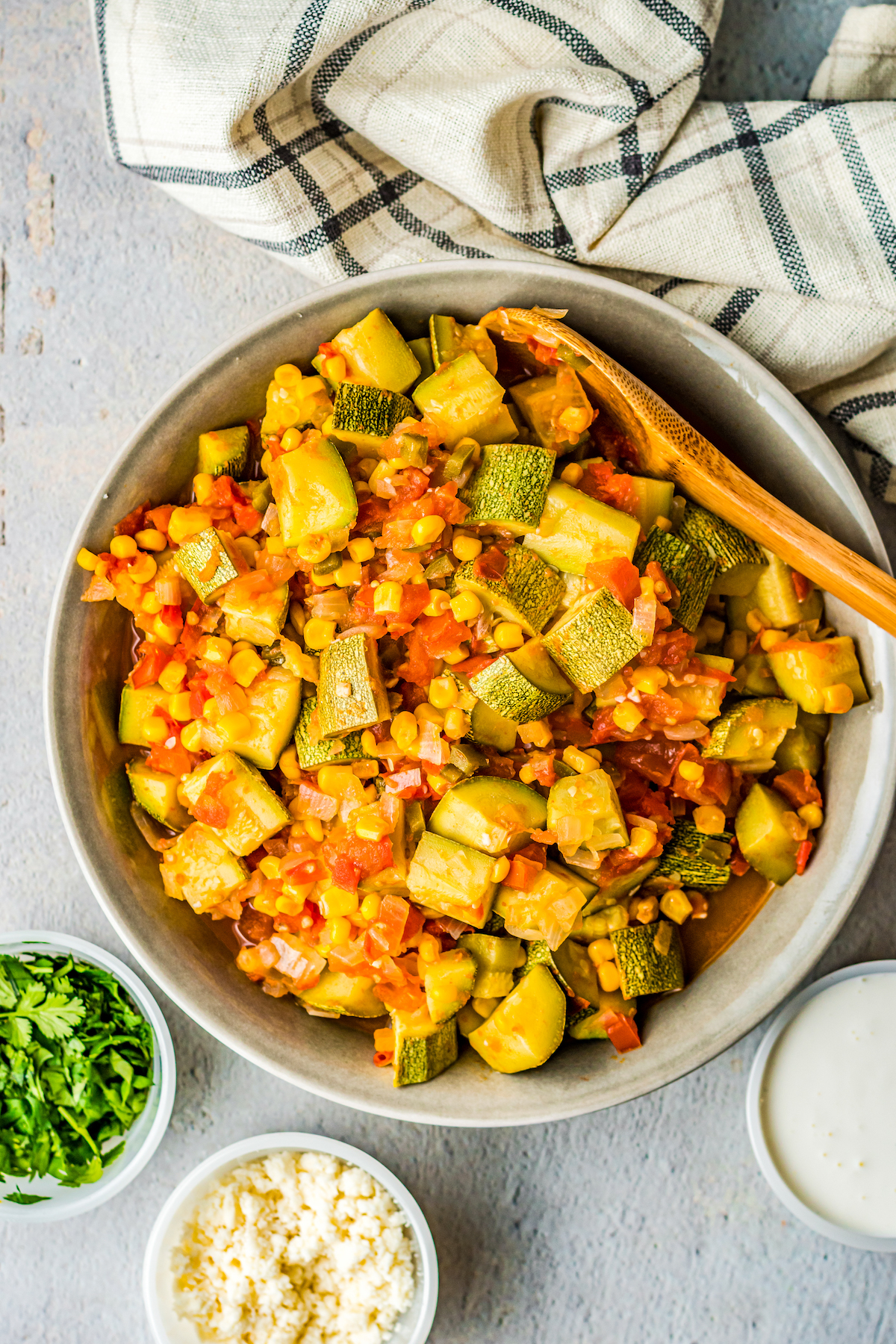 Cooked squash, corn, and tomato medley in a large bowl with a wooden spoon.