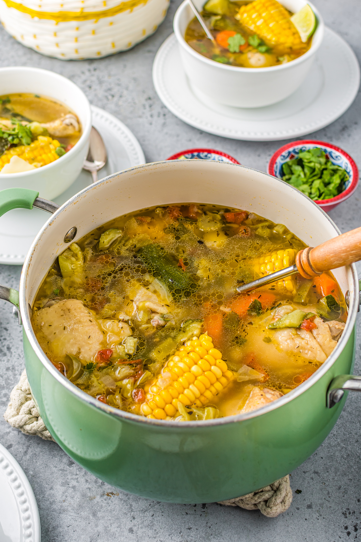 A pot of Mexican chicken stew iwth corn on the cop, pieces of chicken, other vegetables, and herbs