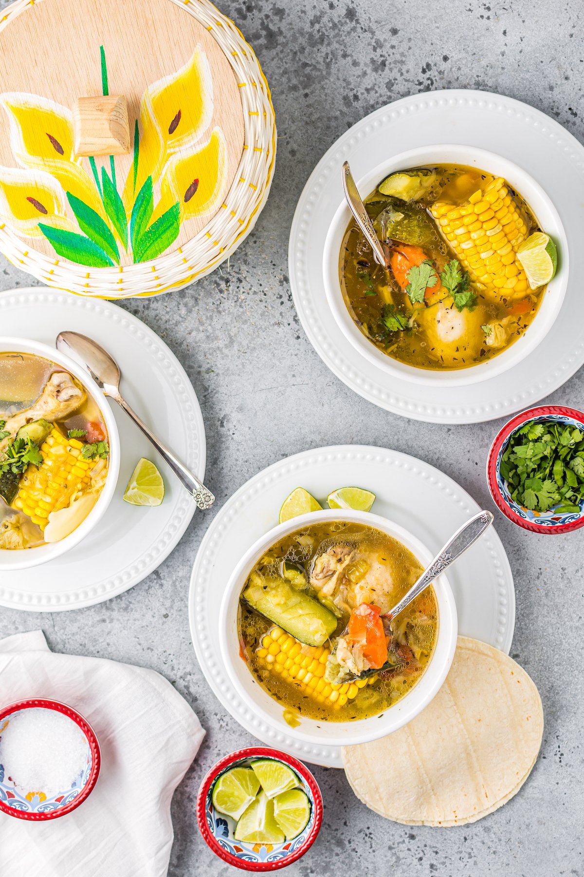 three bowls of Mexican chicken soup that have corn on the cob, zucchini, and other vegetables in each bowl 