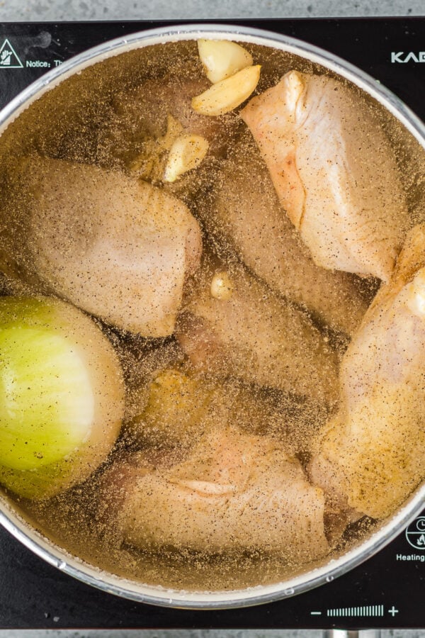 Chicken simmering in water with garlic, onion and seasonings.