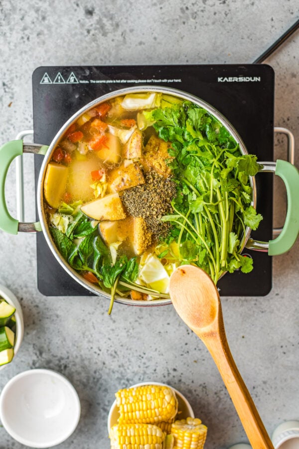 Herbs and seasonings being added to a stock pot of Mexican soup. 