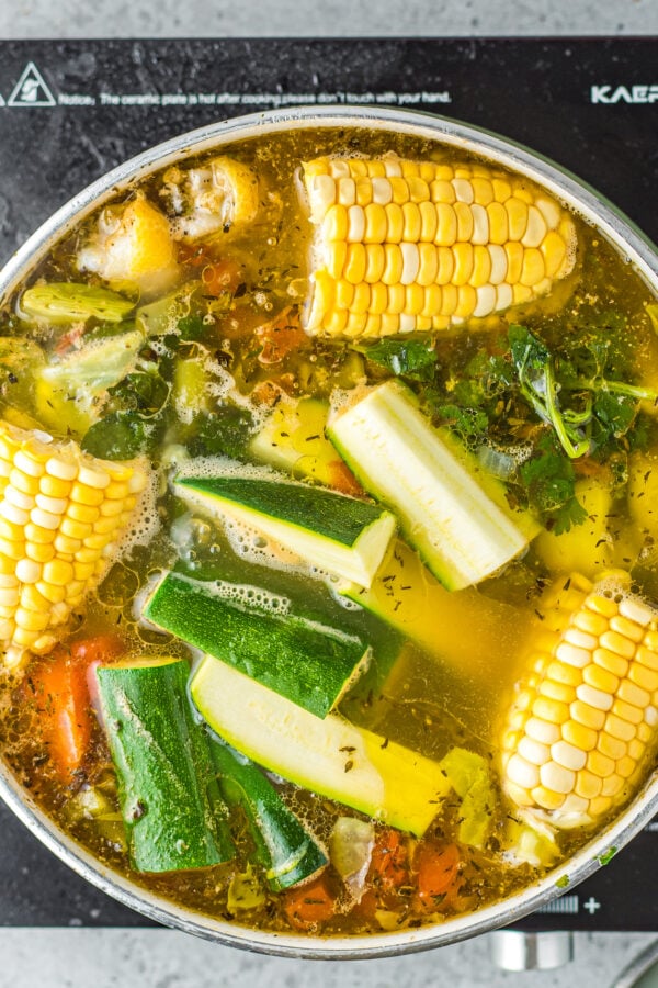 Chicken, corn, potatoes, and fresh herbs in a stockpot.