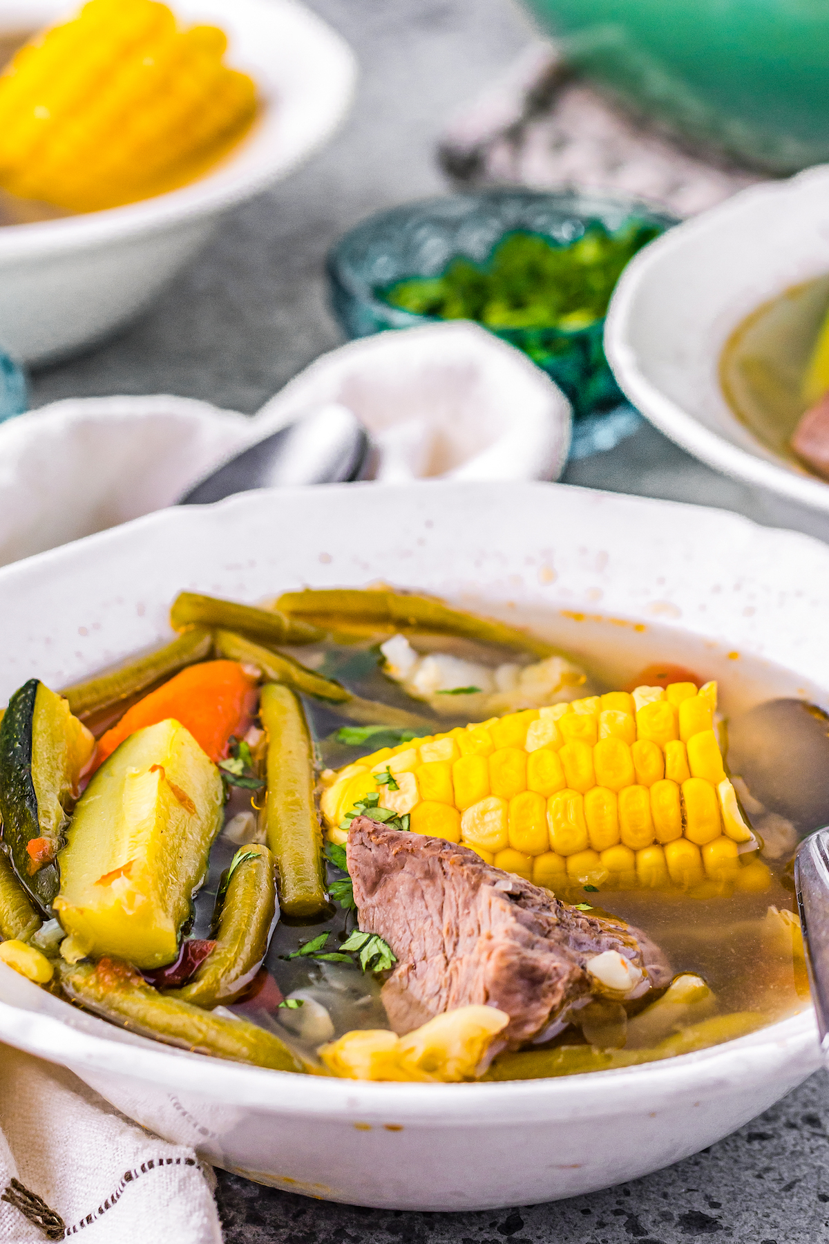 Mexican beef stew with zucchini, corn, fresh herbs, green beans, in a beef-based broth served in a grey bowl