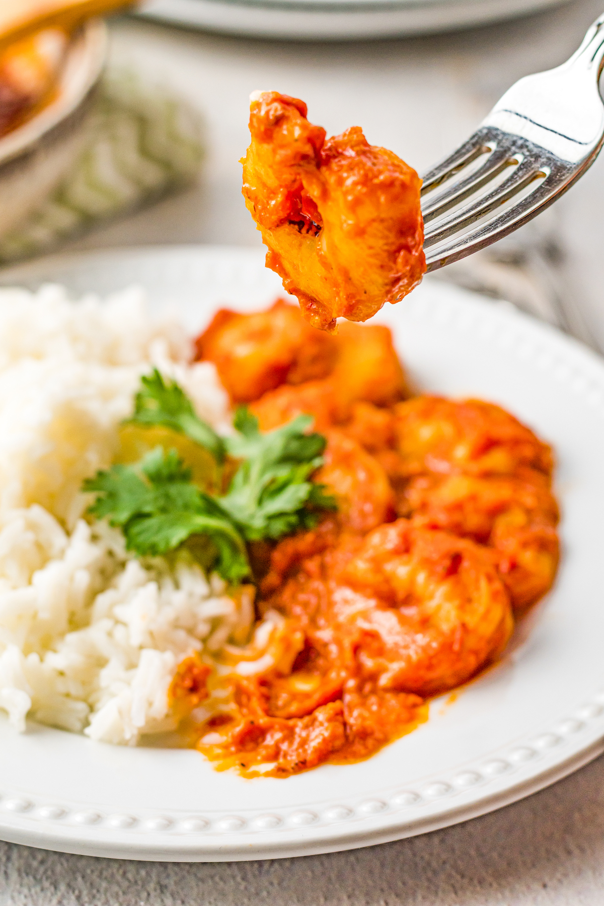 A serving of Mexican deviled shrimp with white rice. One shrimp is being lifted toward the camera on a fork.