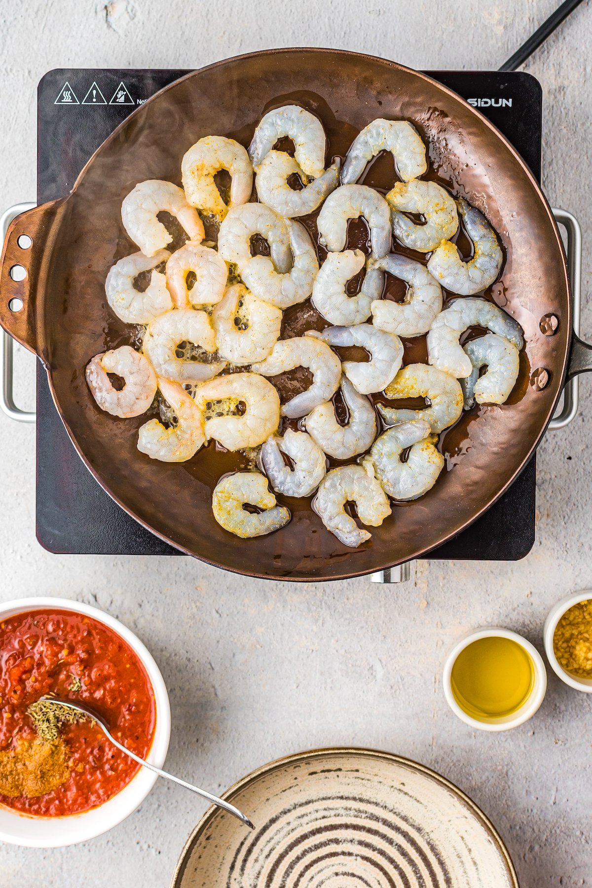 Shrimp cooking in a skillet, with dishes of other ingredients near the skillet.