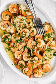 An oval-shaped serving platter with shrimp in a garlic and parsley sauce.