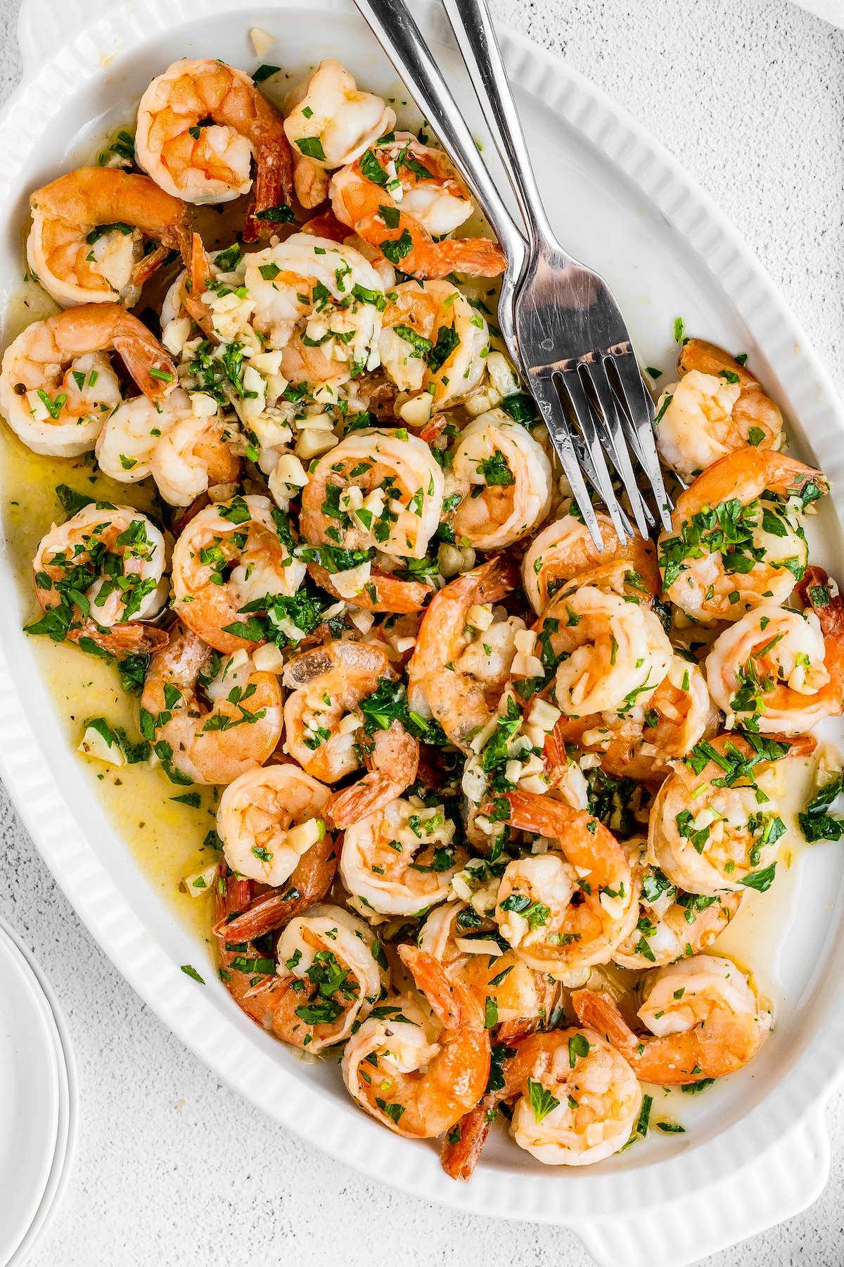 An oval-shaped serving platter with shrimp in a garlic and parsley sauce.