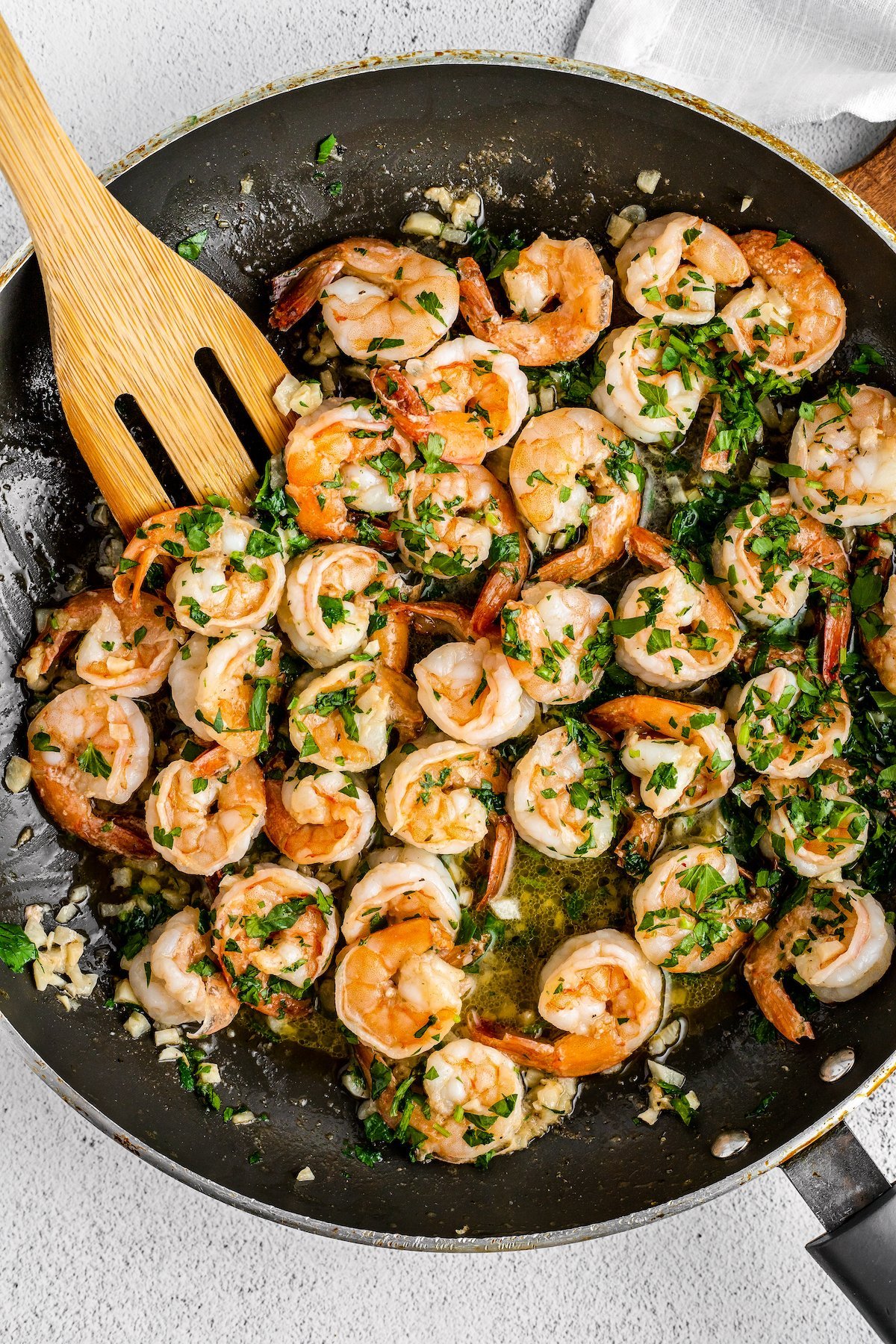 Shrimp in a skillet being stirred with a wooden spatula.