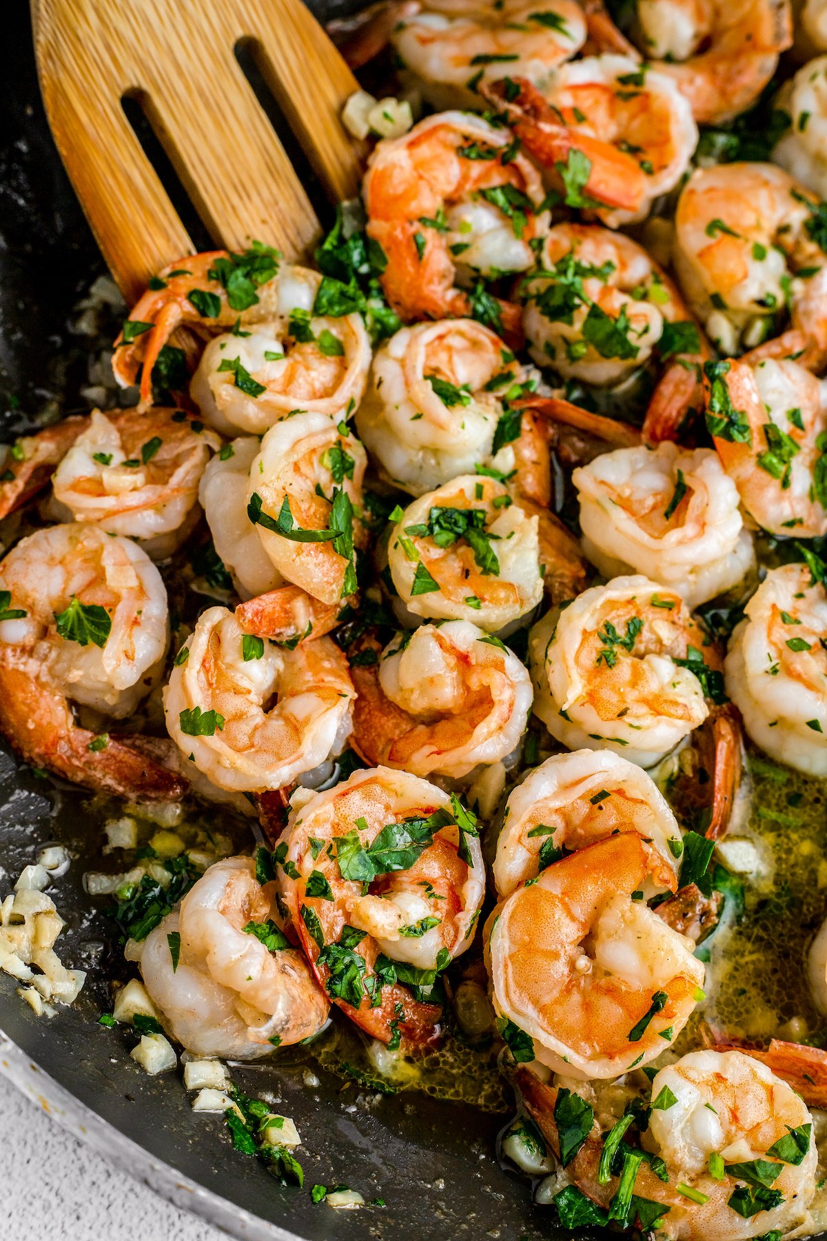 Close-up shot of shrimp in a skillet, sprinkled with parsley and garlic.