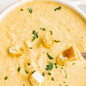 A bowl of low carb cauliflower soup with parsley and bread croutons on top.