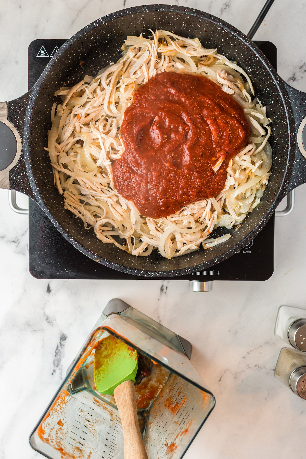 shredded chicken in a cast iron skillet with red sauce poured on top