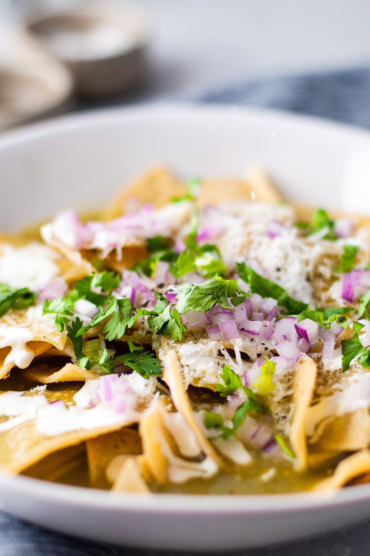 Tortilla chips topped with salsa verde, onions, cilantro, and crema in a white bowl