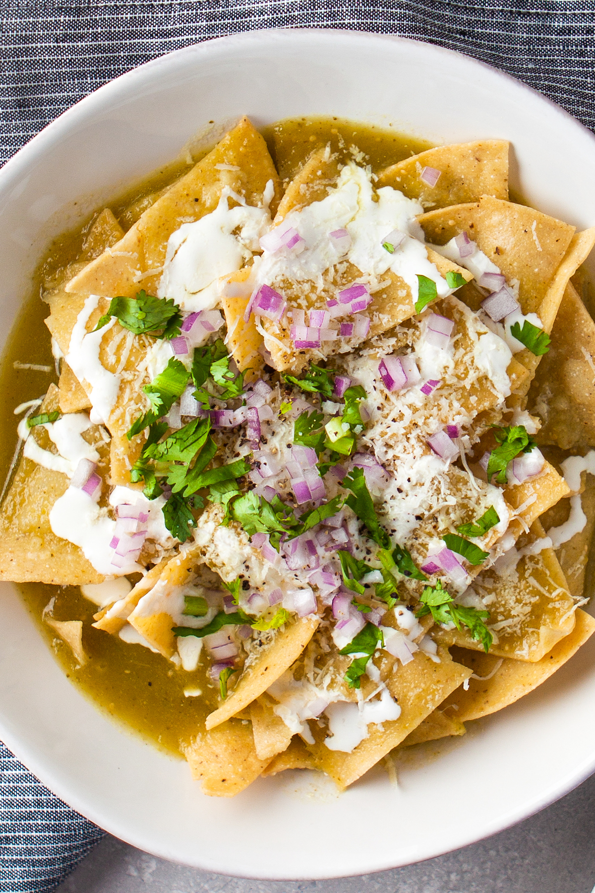 Tortilla chips topped with salsa verde, onions, cilantro, and crema in a white bowl