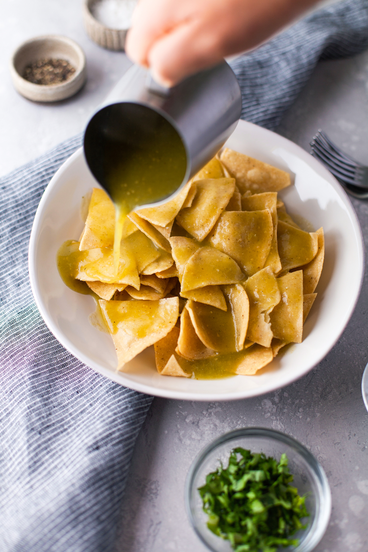 salsa verde being poured on tortilla chips in a white bowl