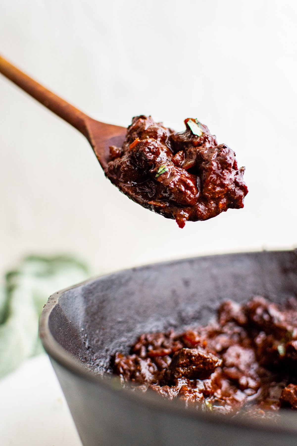  Mexican beef stew made with beef, dried chili peppers, and spices on a spoon above a cast iron skillet