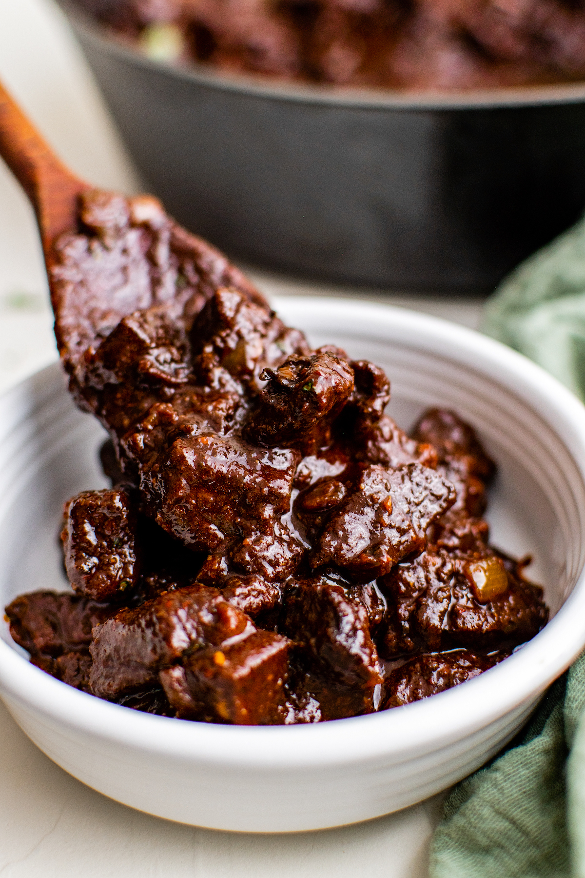  Mexican beef stew made with beef, dried chili peppers, and spices being served in a bowl by a wooden spoon.