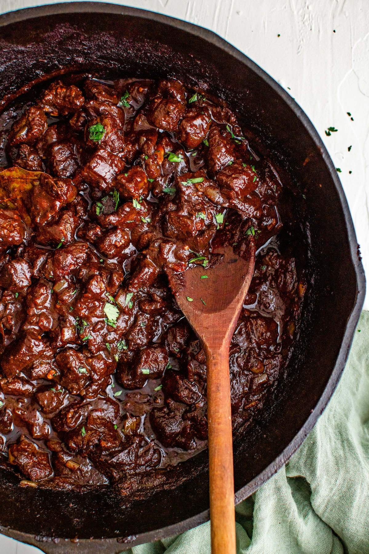  Mexican beef stew made with beef, dried chili peppers, and spices being mixed in a cast iron skillet