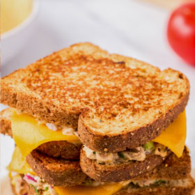 Tuna melt sandwiches stacked on top of each other on a piece of parchment paper.