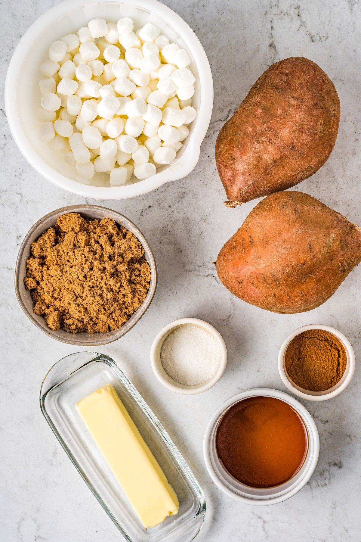 a counter with sweet potatoes, bowl of marshmallows, brown sugar, butter, salt, pumpkin pie spice,maple syrup, mini marshmallows, and cinnamon