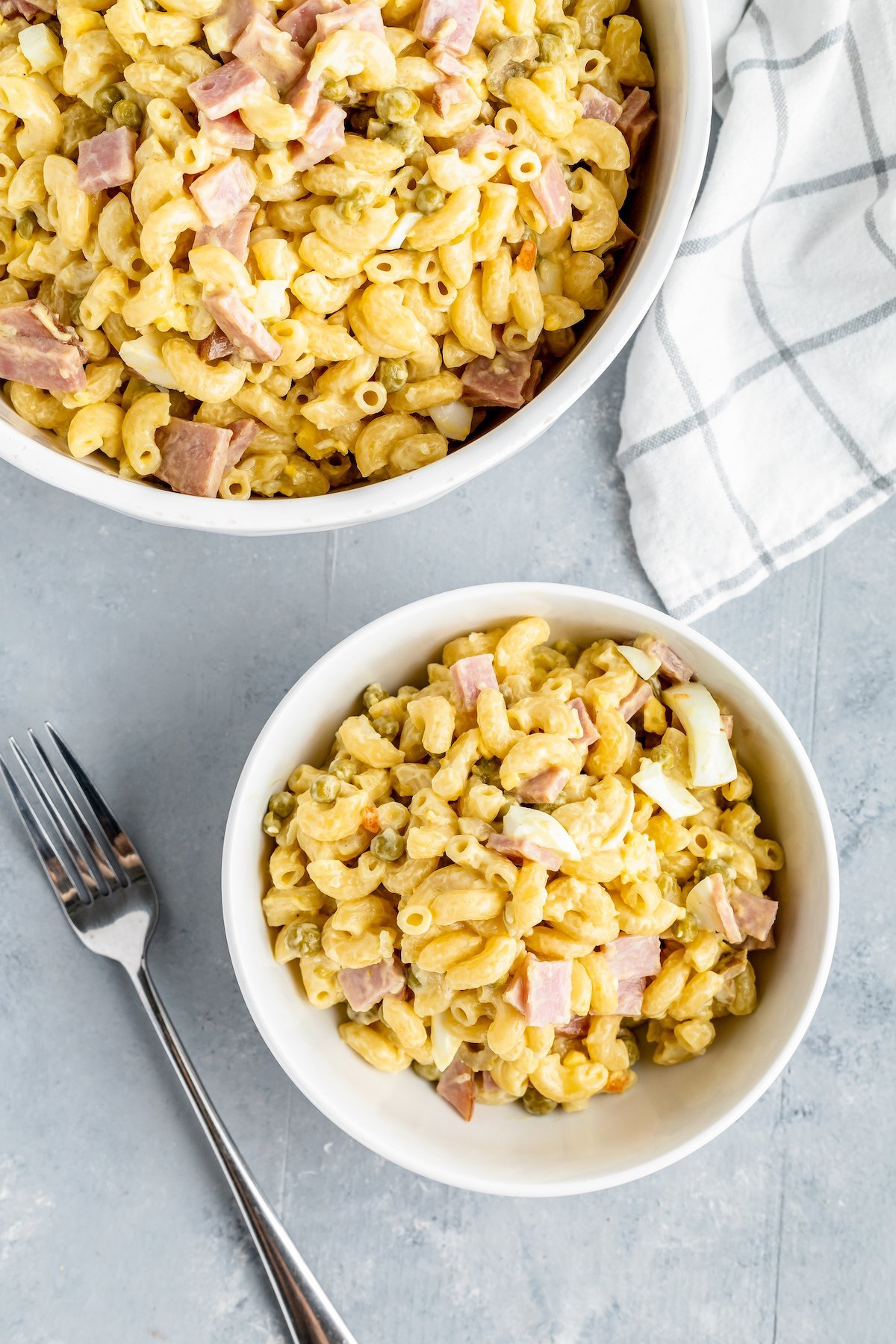 Overhead shot of a serving bowl of ensalada de conditos con jamon, next to a smaller bowl of the same macaroni salad. A fork is next to the smallest bowl.