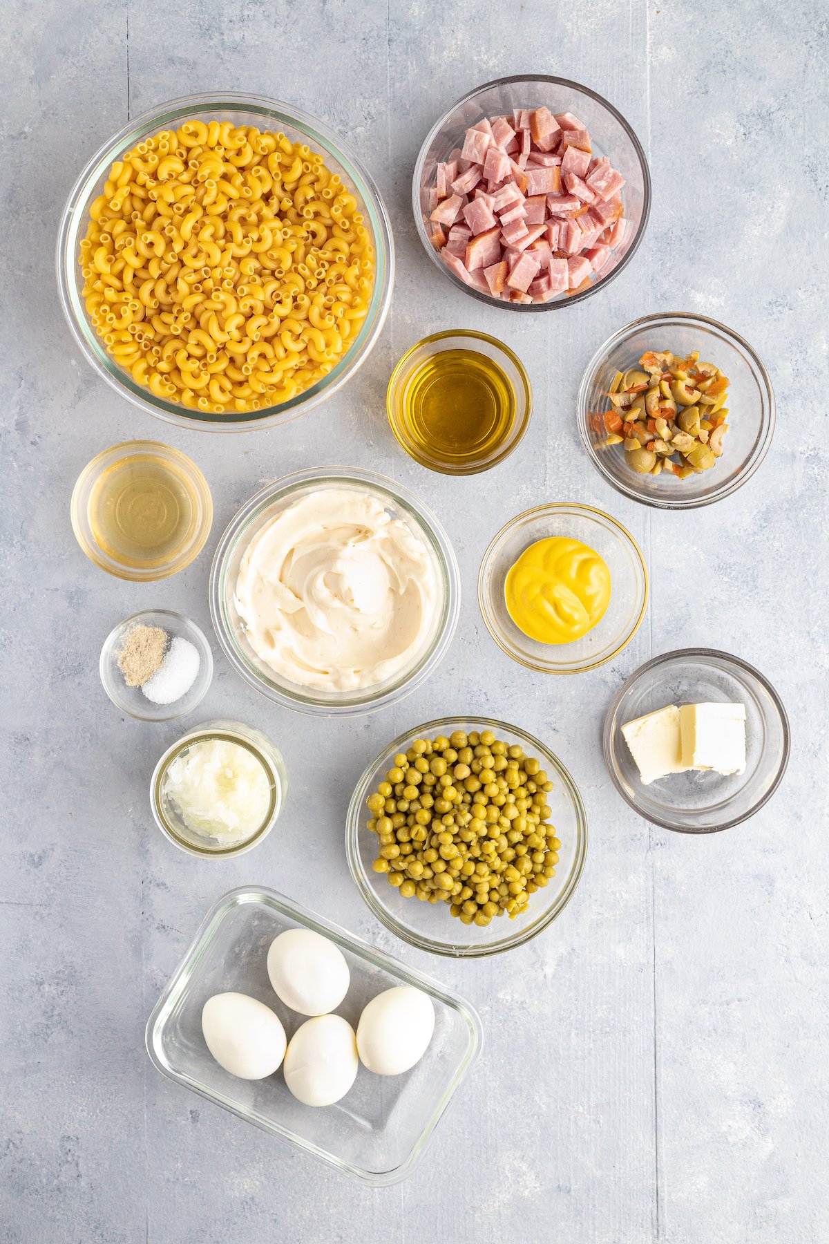 From top left: Elbow pasta, chopped ham, pimiento juice, olive oil, sliced olives, mayonnaise, mustard, salt and white pepper, grated onion, peas, butter, hard boiled eggs.
