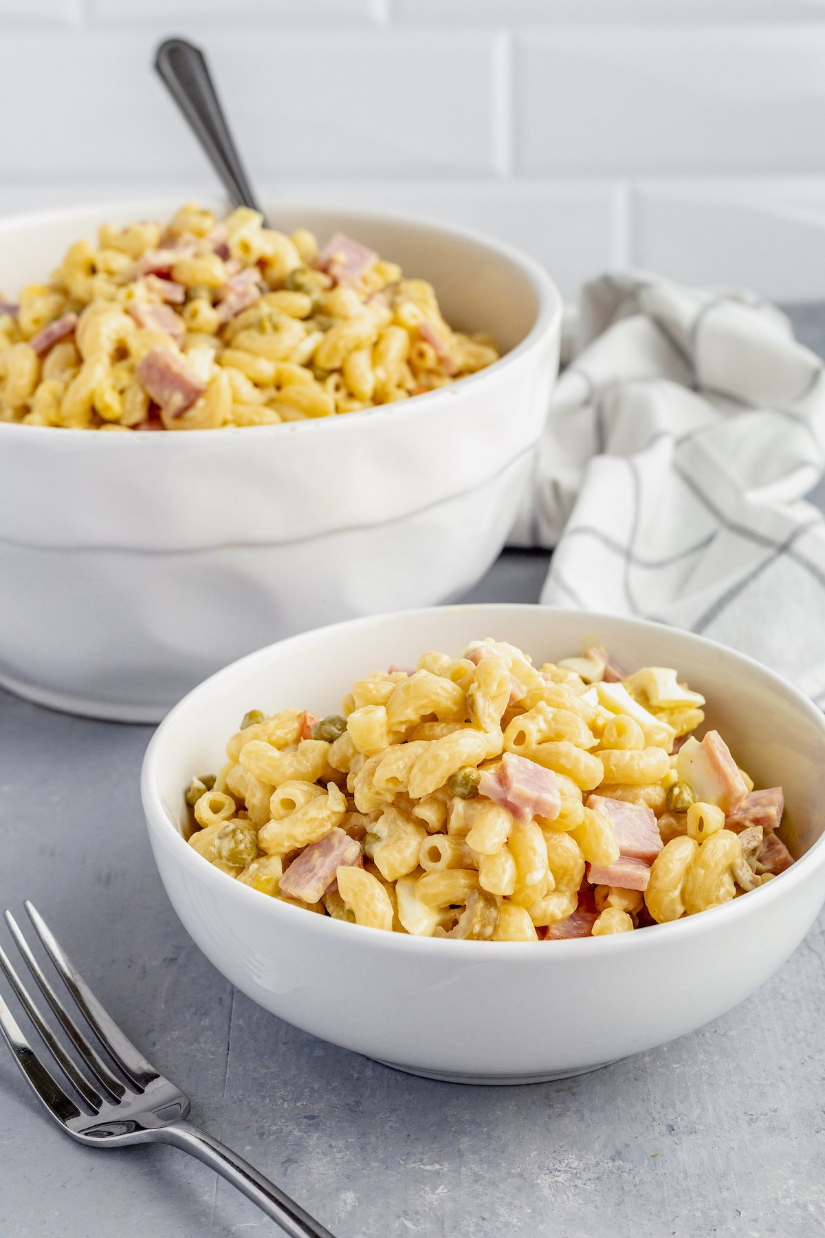 A serving of Puerto Rican pasta salad next to a larger bowl of the salad.