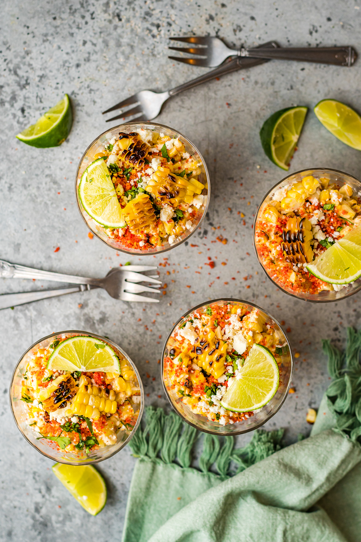 Small cups of Mexican corn salad topped with lime wedges and other toppings.