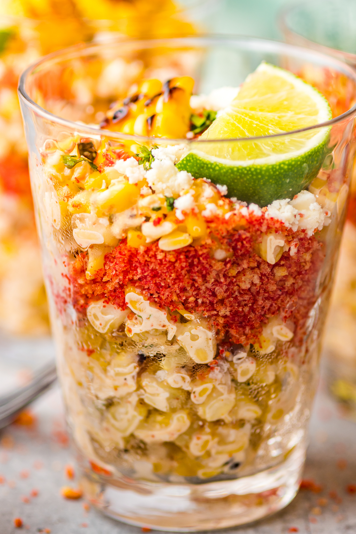 Side view of Mexican corn salad in a cup, showing the layers of corn, crushed hot Cheetos, and other toppings.
