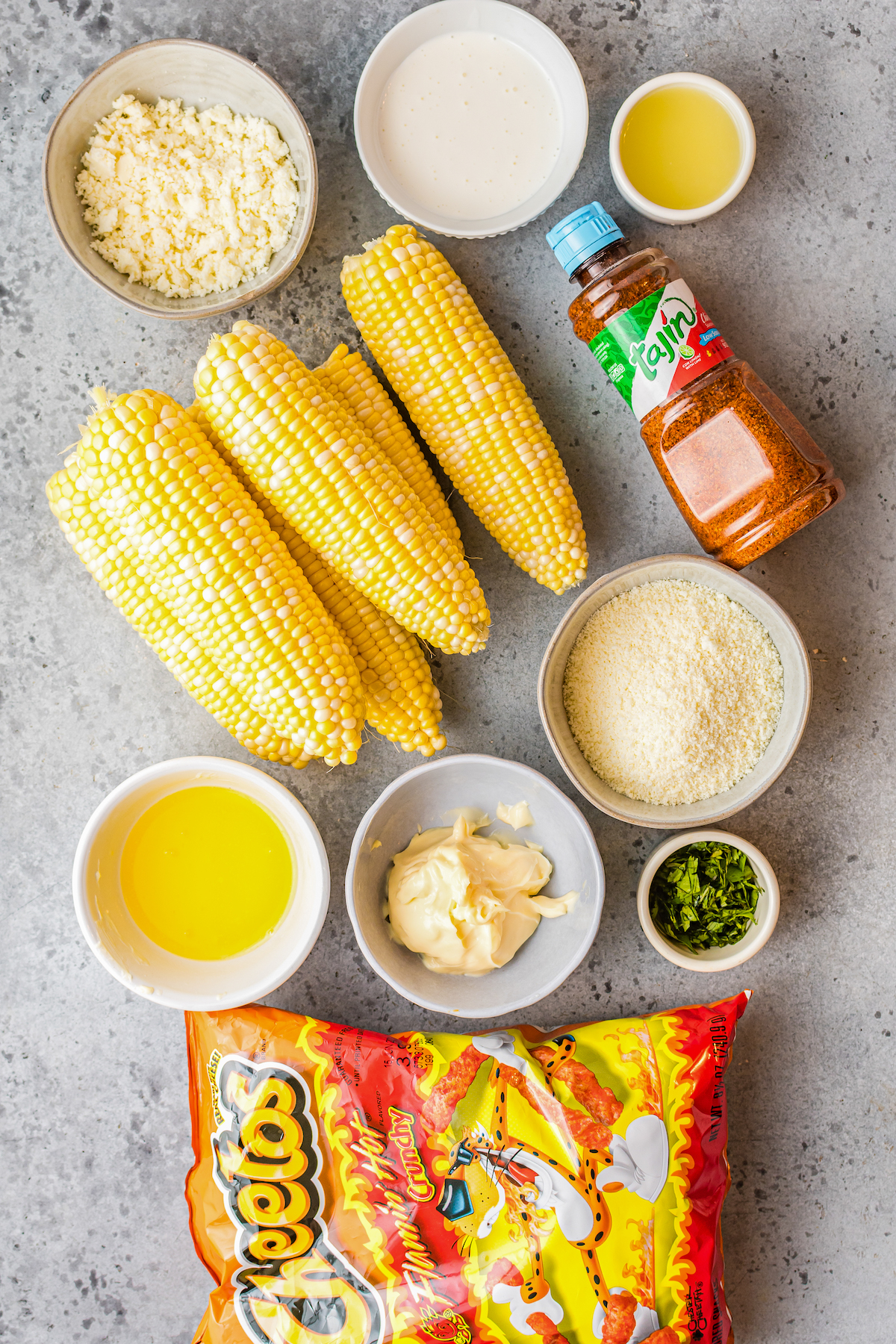 From top left: Cotija crumbles, crema, lime juice, fresh corn on the cob, tajin seasoning, melted butter, queso fresco, cilantro, mayonnaise, and hot Cheetos.