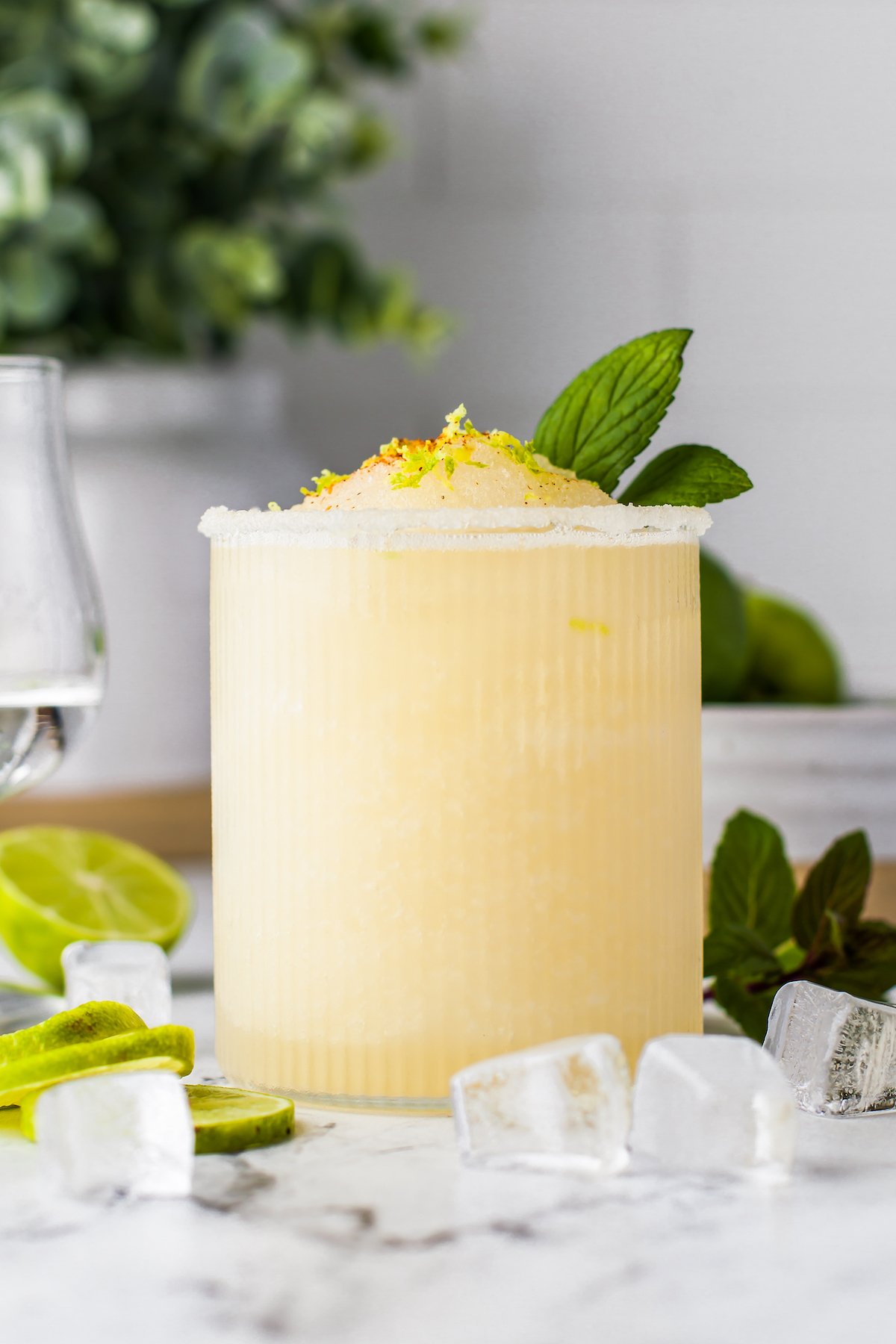 a frozen margarita in a glass with mint and chili spice garnish