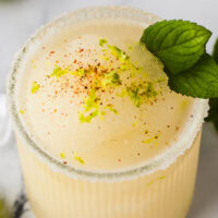 a frozen margarita in a glass with mint and chili spice garnish
