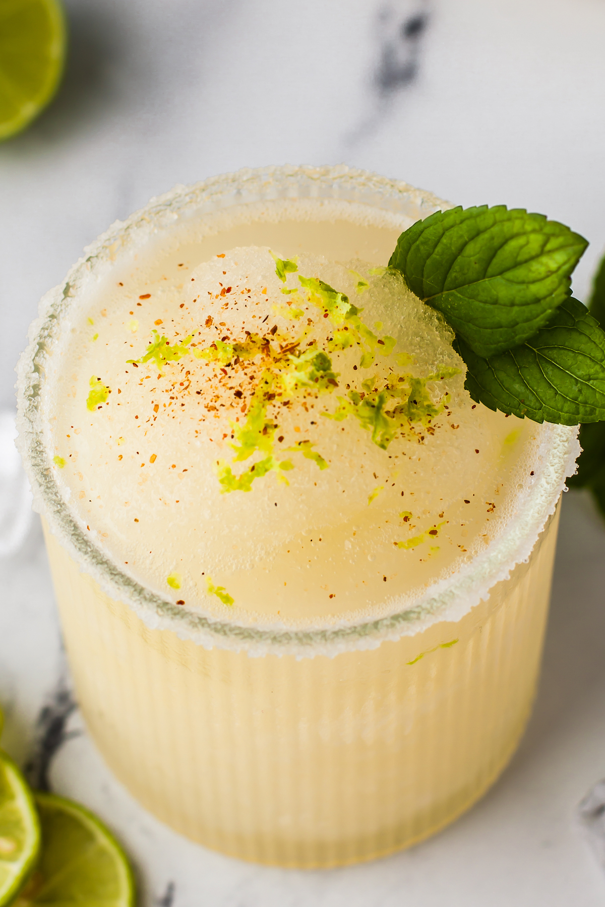 a frozen margarita in a glass with mint and chili spice garnish